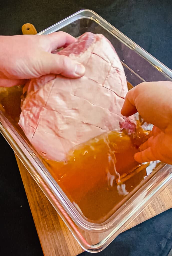 pork shoulder being placed into a container of apple juice brine