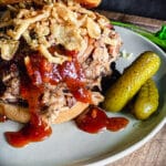 pulled pork sandwich on a plate with bbq sauce and pickles