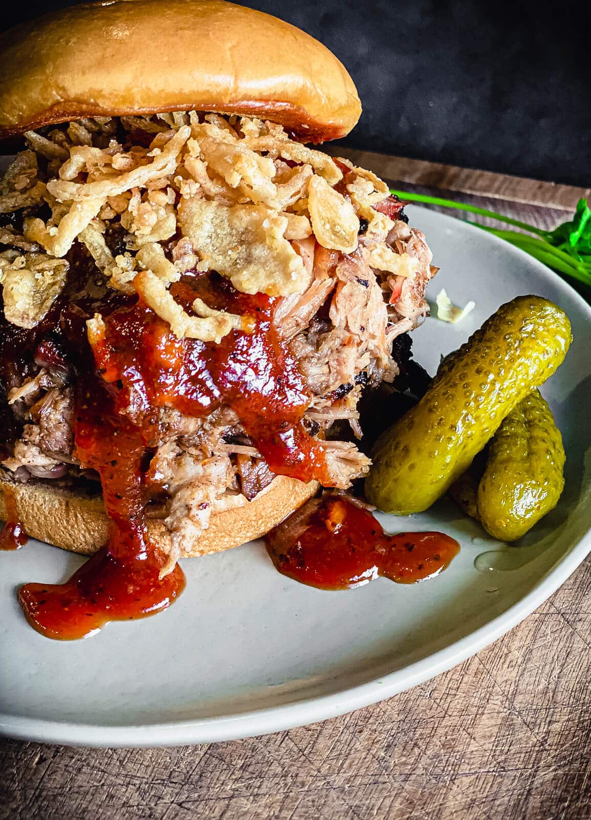 pulled pork sandwich on a plate with bbq sauce and pickles