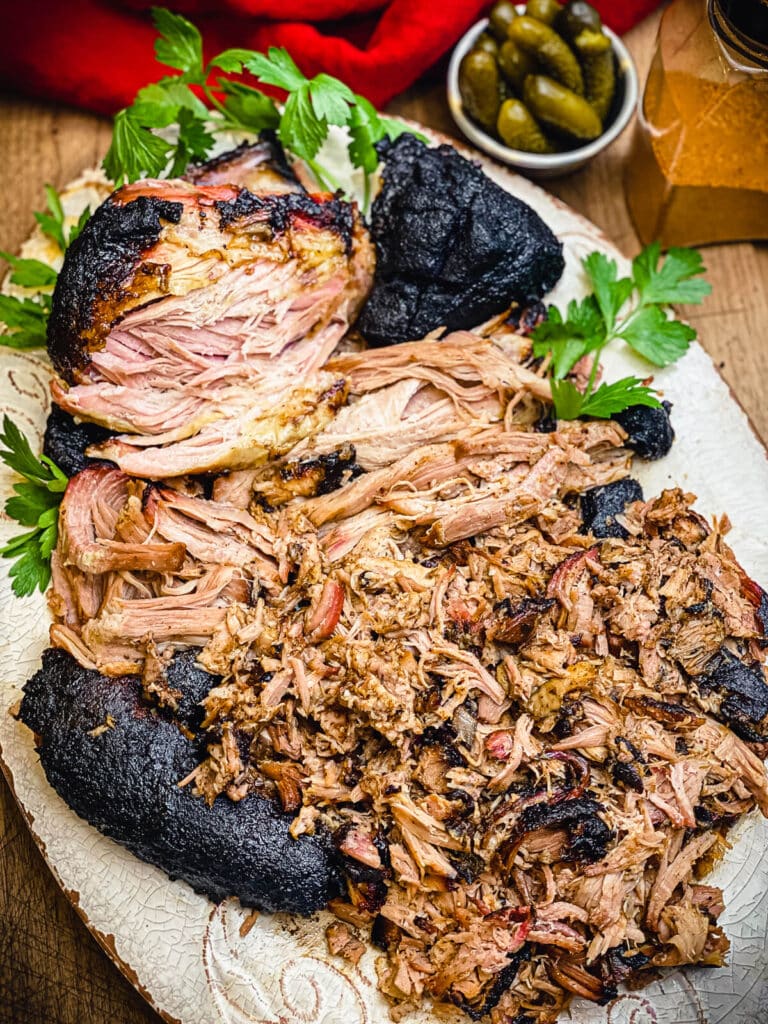pork shoulder pulled apart on a platter with pickles in the background