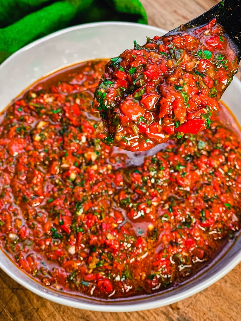 a spoon full of red chimichurri over a bowl of sauce