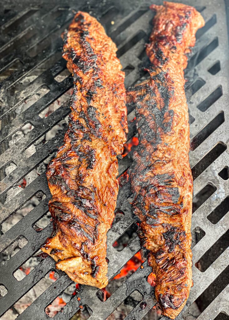 charred skirt steak on a grill over hot coals