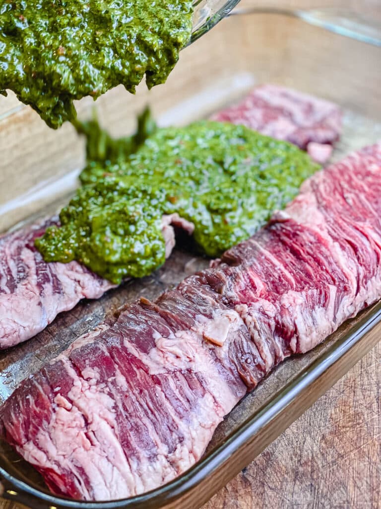 chimichurri sauce being poured over top of skirt steaks