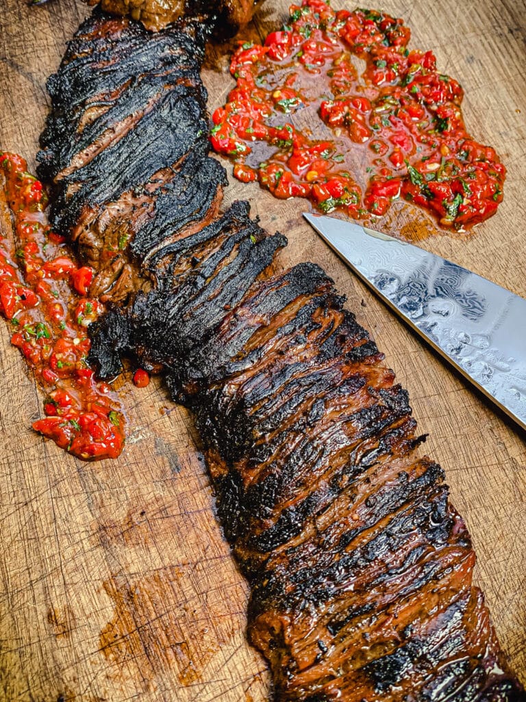 charred skirt steak on a cutting board with red chimichurri
