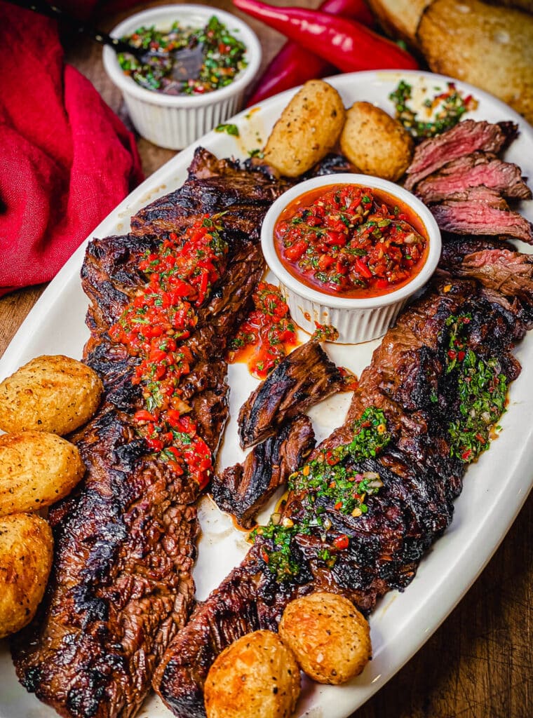 churrasco steak on a white platter with chimichurri and potatoes