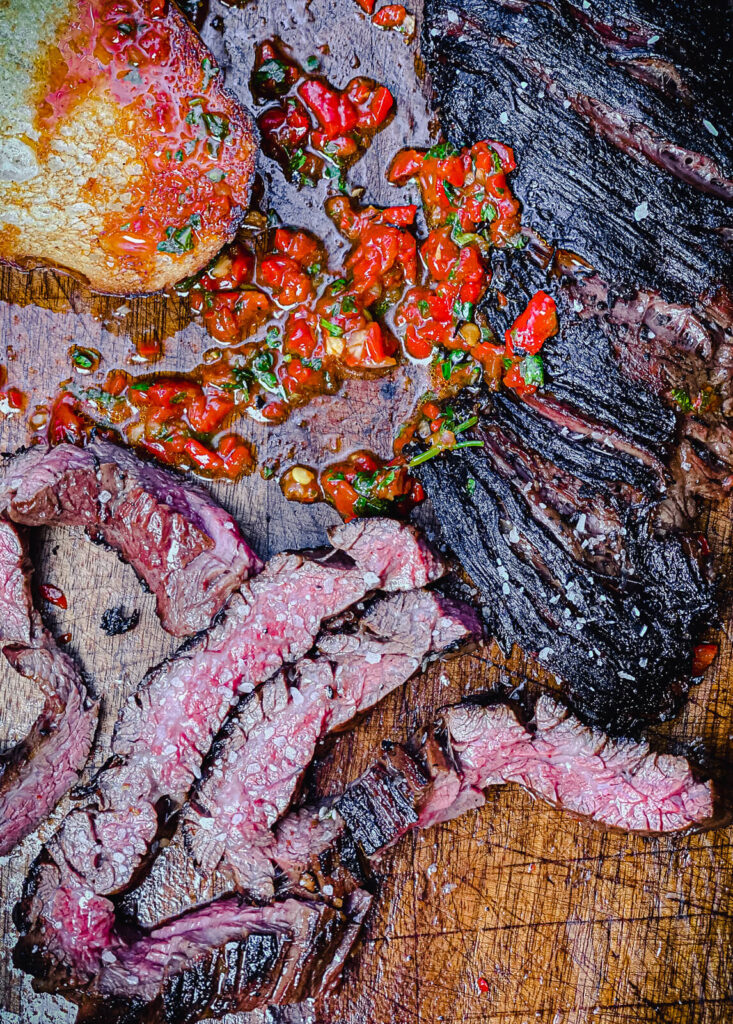 sliced skirt steak on a cutting board with red chimichurri