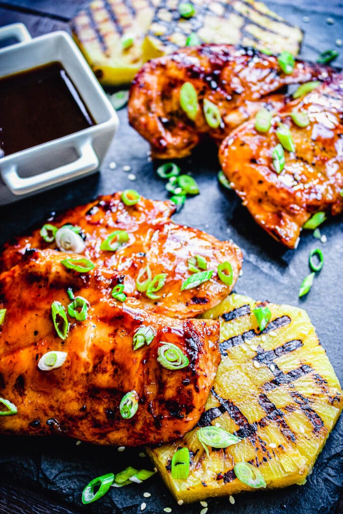 Hawaiian huli huli chicken thighs on a cutting board with grilled pineapple