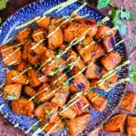 roasted sweet potatoes on a blue plate drizzled with avocado cream sauce