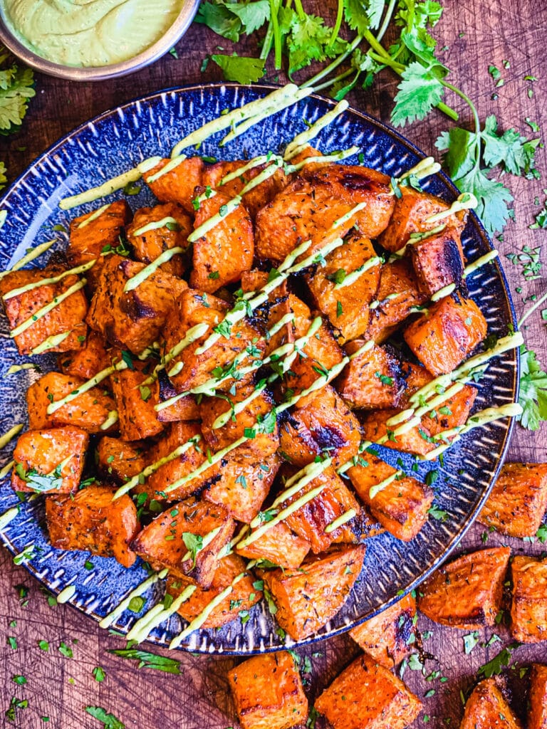 roasted sweet potatoes on a blue plate drizzled with avocado cream sauce