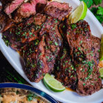 sliced flap meat on a white platter with limes and a salad