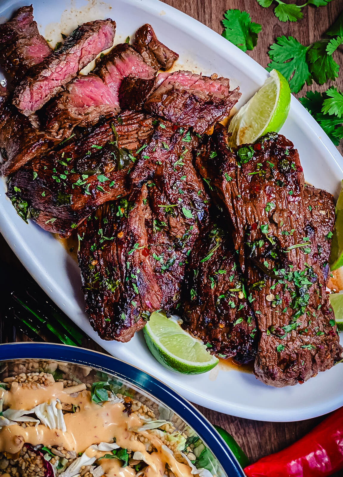 sliced flap meat on a white platter with limes and a salad