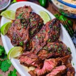 sliced flap steak on a platter with sauce and limes