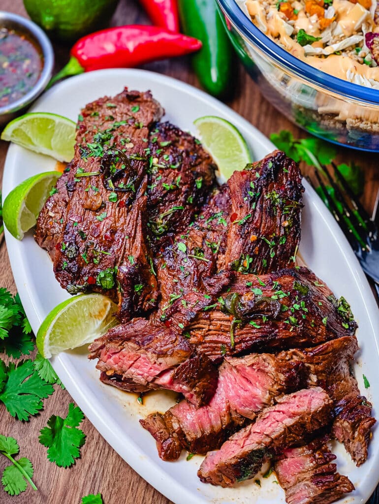 sliced flap steak on a platter with sauce and limes
