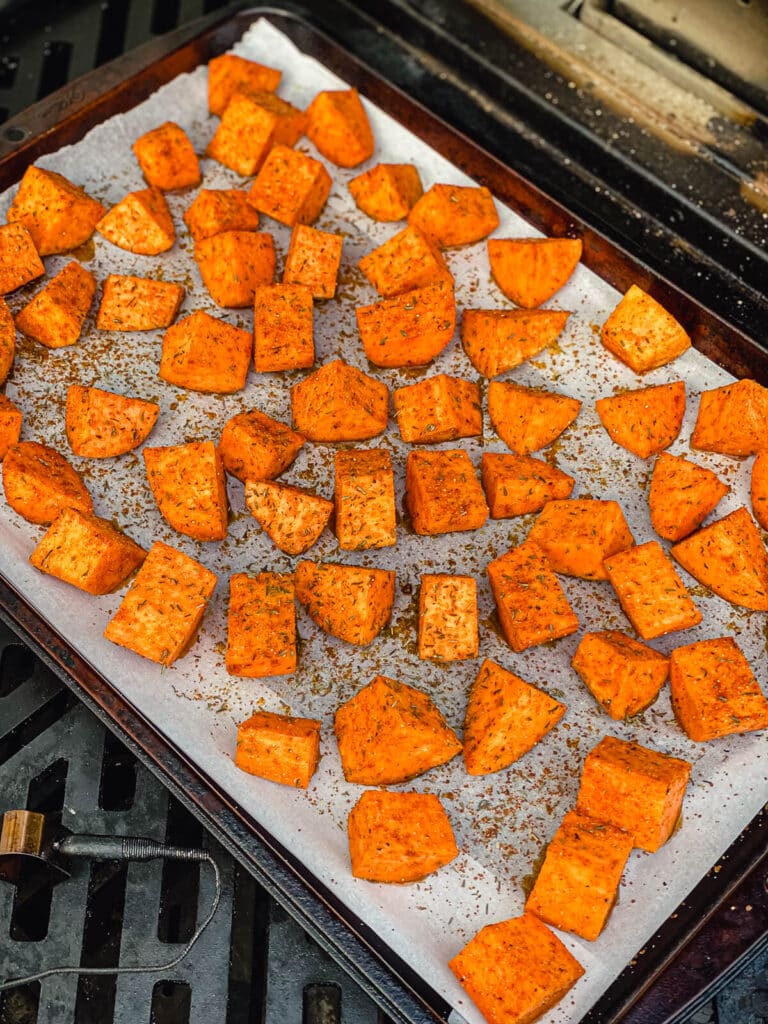 sweet potatoes on a parchment lined baking sheet roasting on a grill.