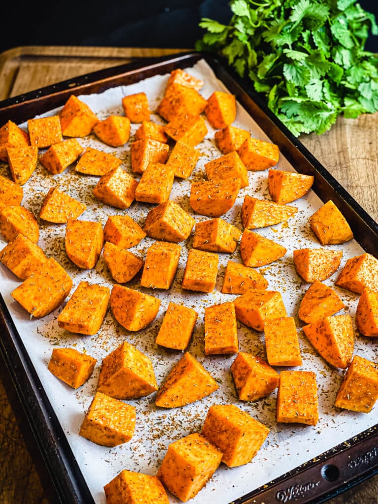 seasoned sweet potatoes on a parchment lined baking sheet