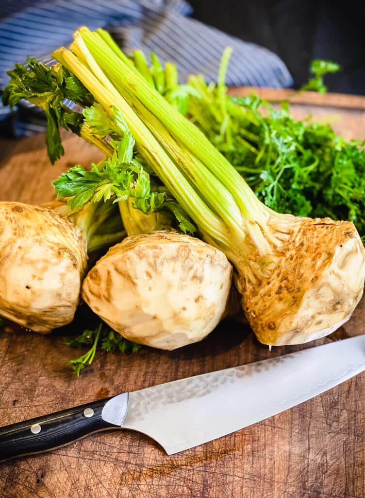 whole celery roots with stalks on a cutting board