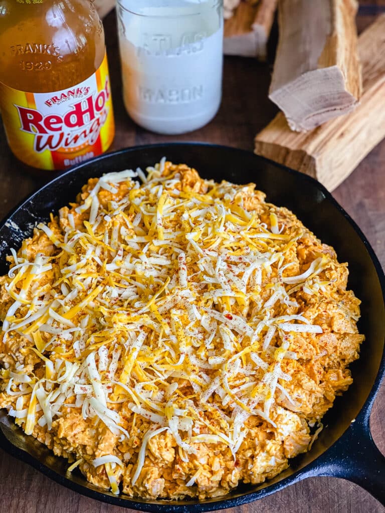 ingredients for smoked buffalo chicken dip assembled in a cats iron pan with Franks RedHot Sauce