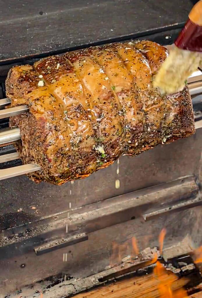 basting a prime rib roast while it's on the rotisserie over a fire