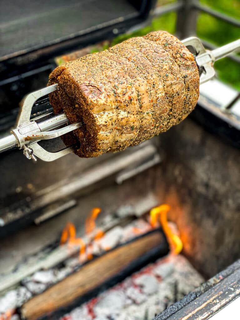 prime rib roast on a rotisserie spit over a fire on a grill