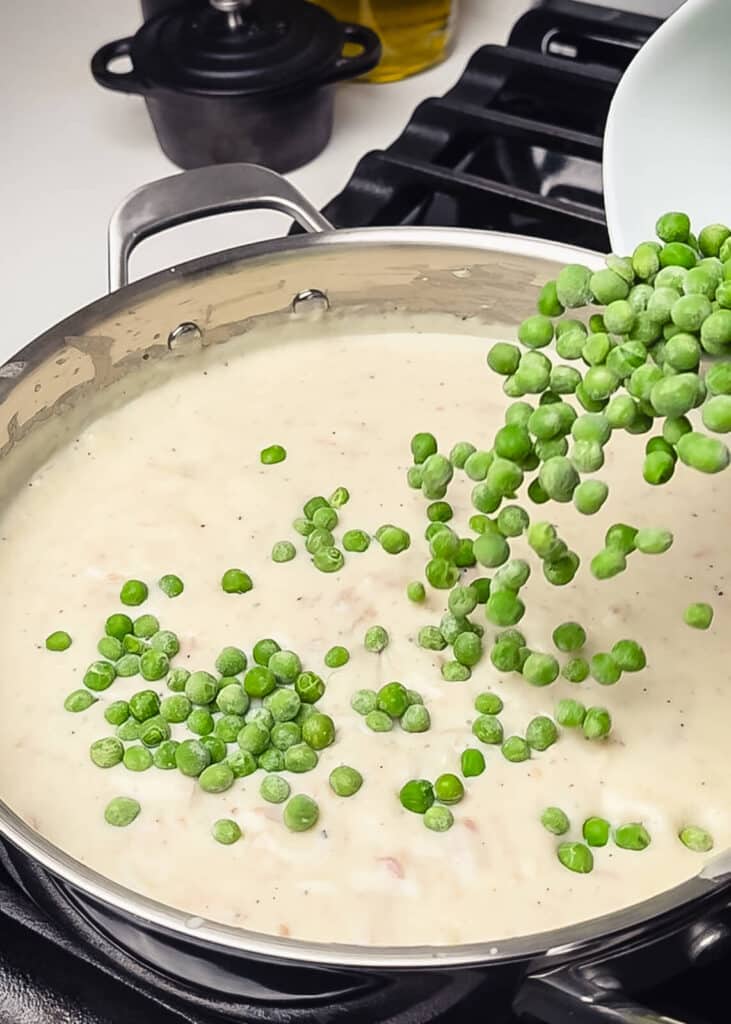 peas being added into a creamed tuna recipe in a pan