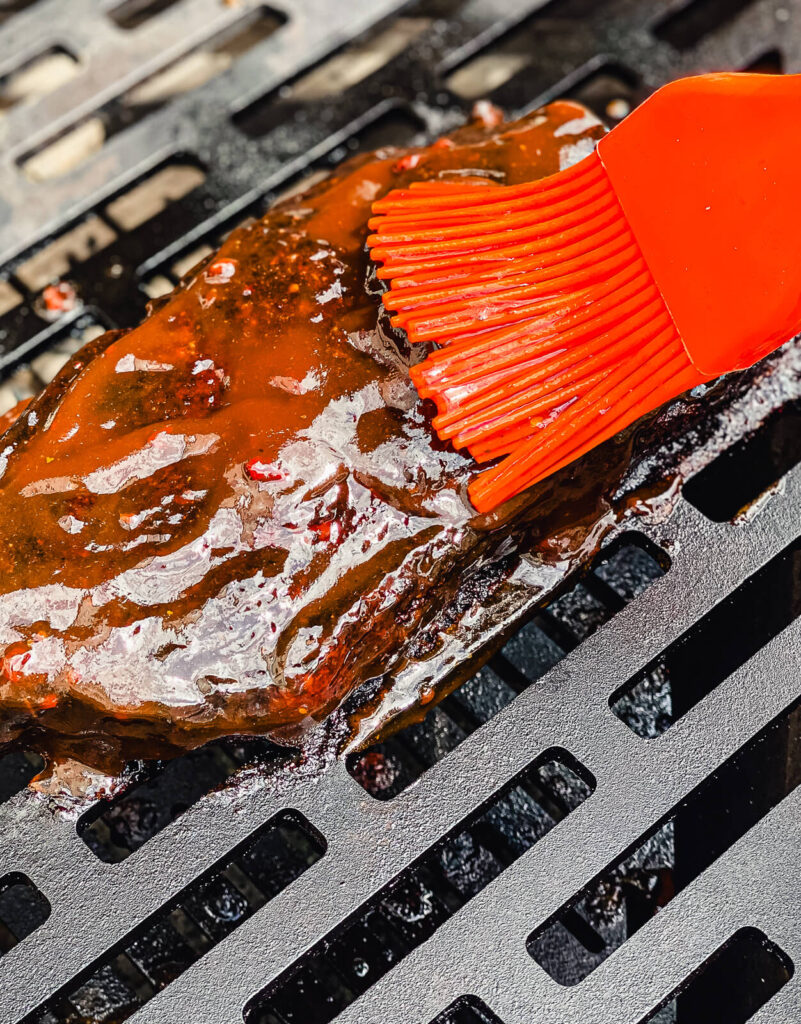 basting brush applying bbq sauce to pork on a grill