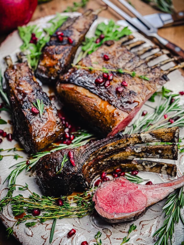 grilled rack of lamb chops on a platter with herbs and pomegranate