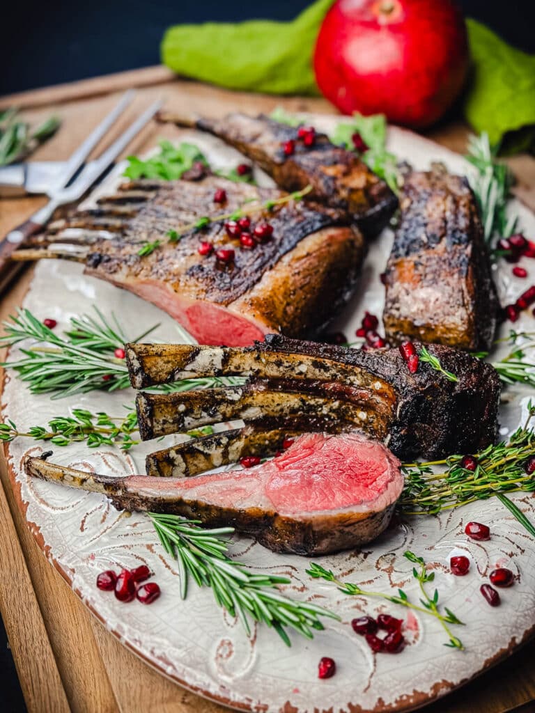 grilled rack of lamb recipe displayed on a platter with herbs and pomegranate seeds