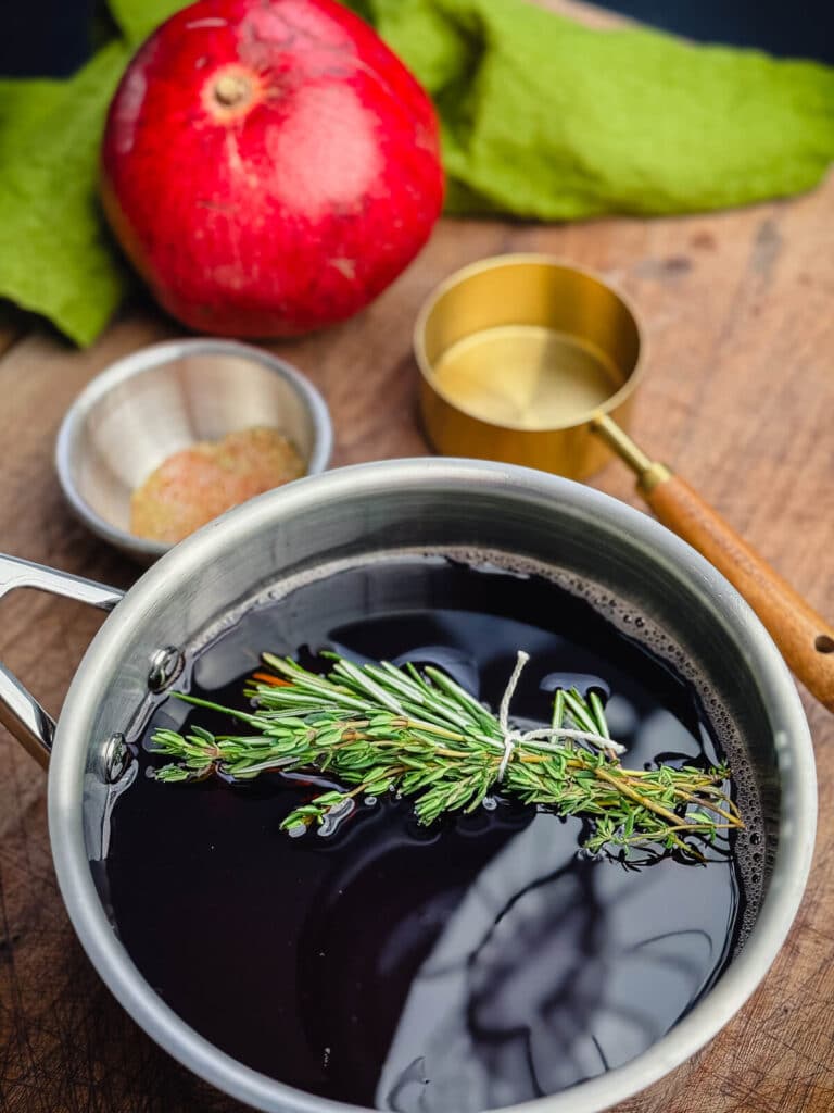 herbs floating in pan of pomegranate glaze