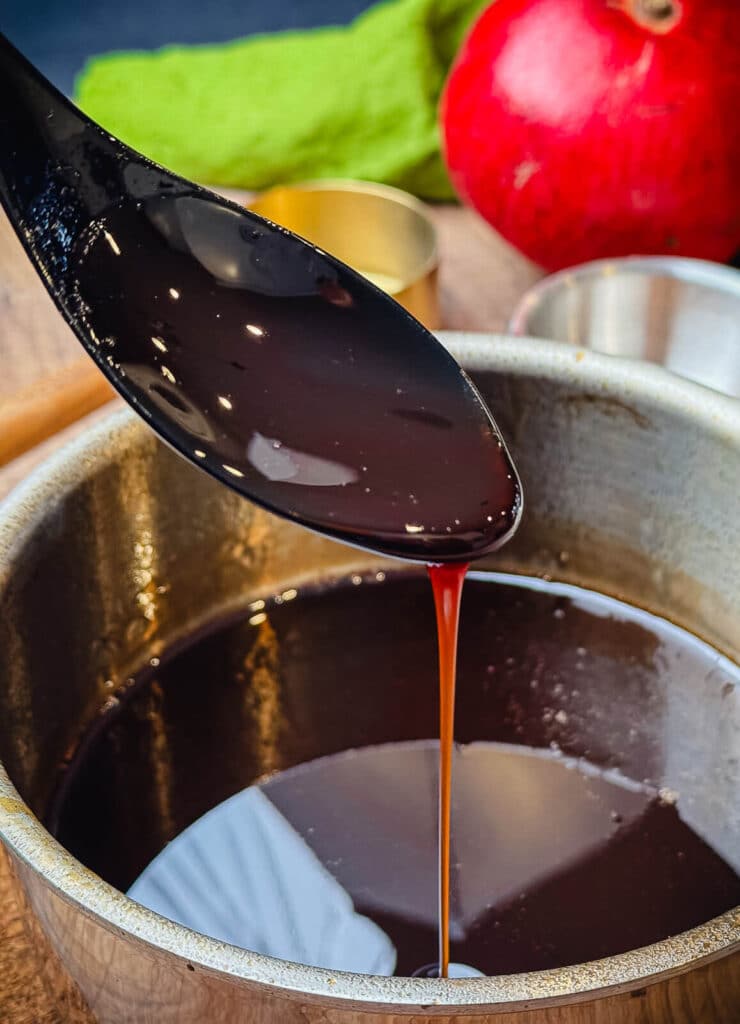 pomegranate glaze dripping from a spoon into a saucepan full of glaze