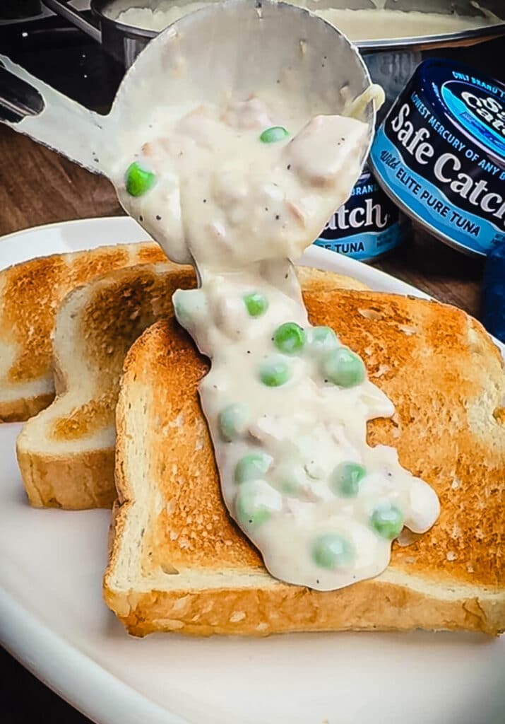 creamed tuna being poured over toast on a white plate