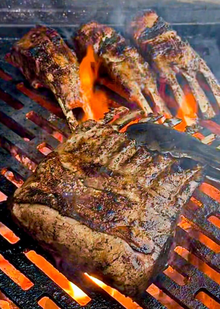 rack of lamb on a grill being held by a pair of tongs