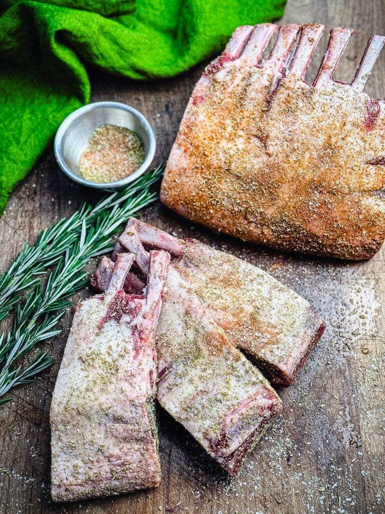 seasoned rack of lamb on a cutting board with herbs