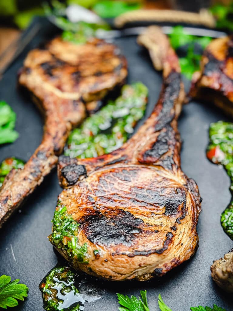 close up of bone-in pork chops on a cutting board with bright green sauce