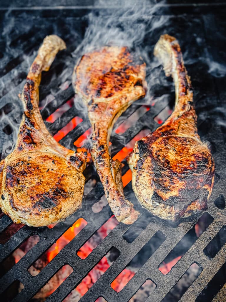 tomahawk pork chops on a grill over hit coals