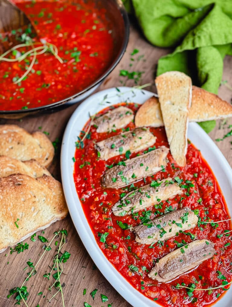 Sardines fra diavolo on a platter with bread and herbs