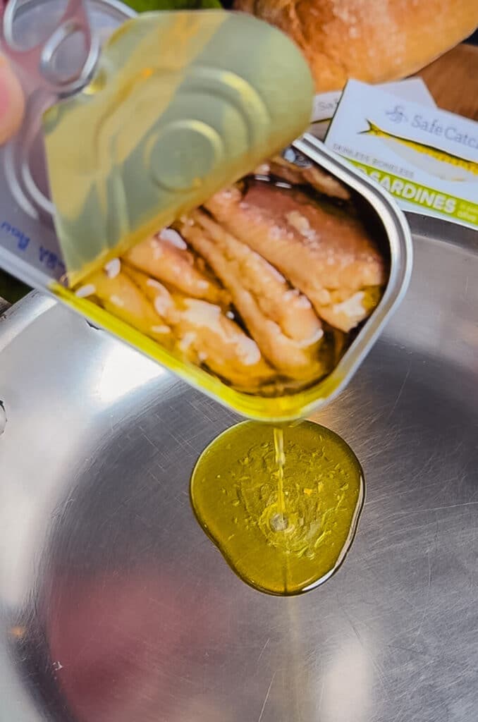 oil pouring from a sardine can into a skillet