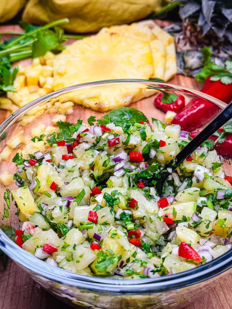 spoon in a bowl with bright pineapple, cilanto, and chilis