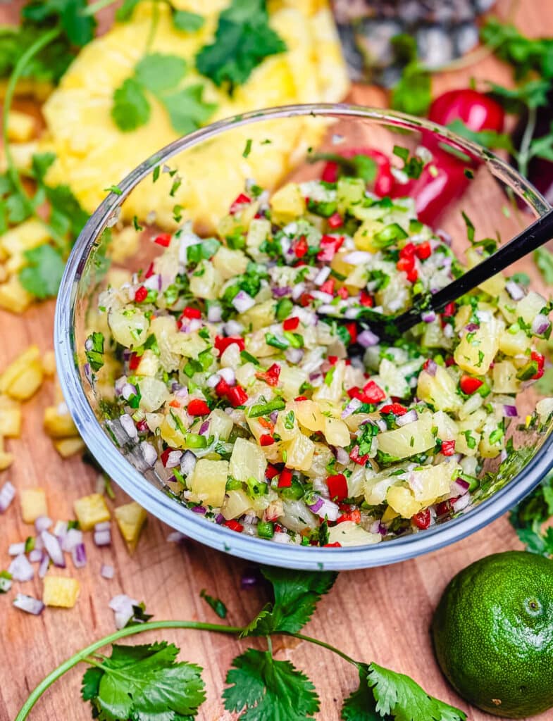 glass bowl of pineapple salsa with black spoon and cilantro