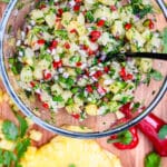 bowl of pineapple salsa on a wood cutting board with a black spoon