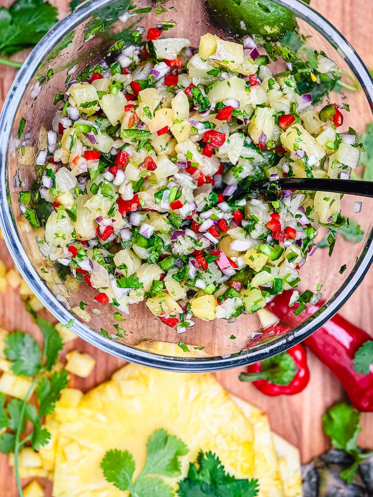 bowl of pineapple salsa on a wood cutting board with a black spoon