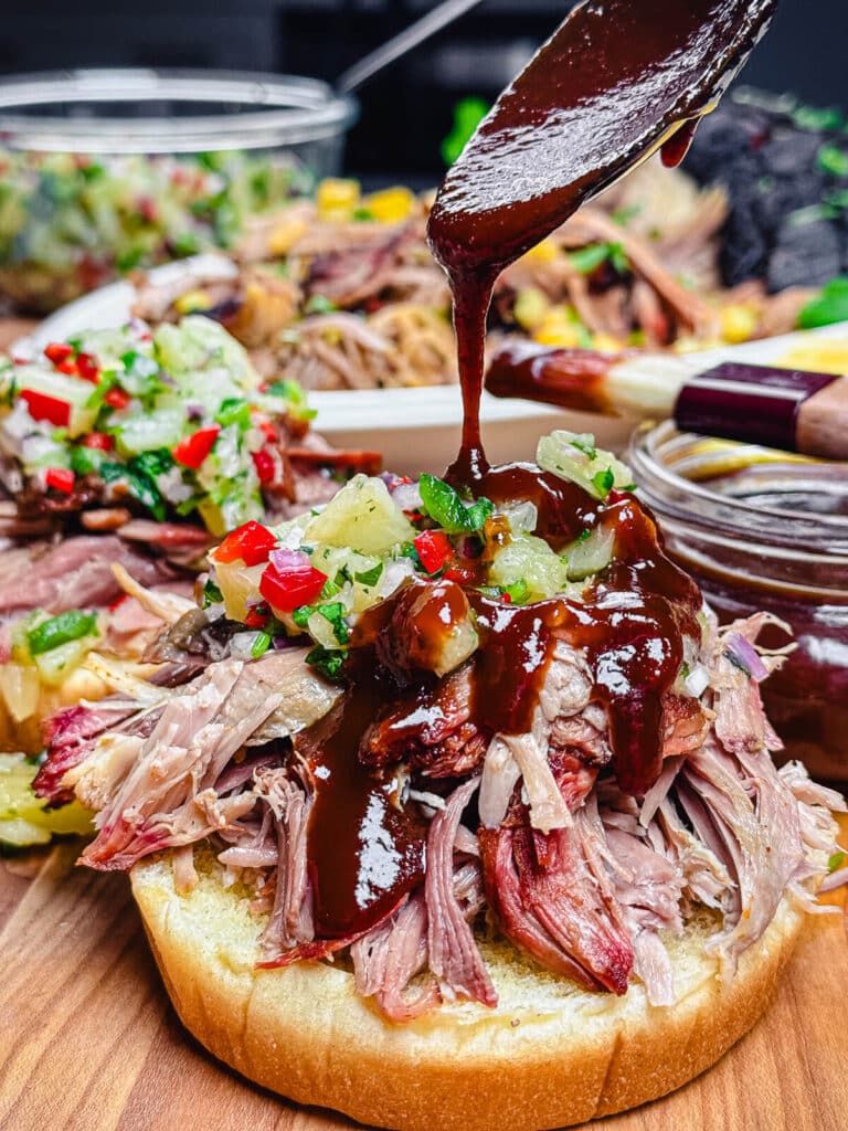 bbq sauce being added to a pulled pork sandwich