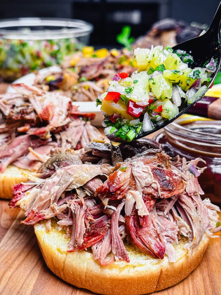 pineapple salsa being added to a pulled pork sandwich