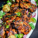 white platter full of chipotle chicken thighs, limes, and jalapeños