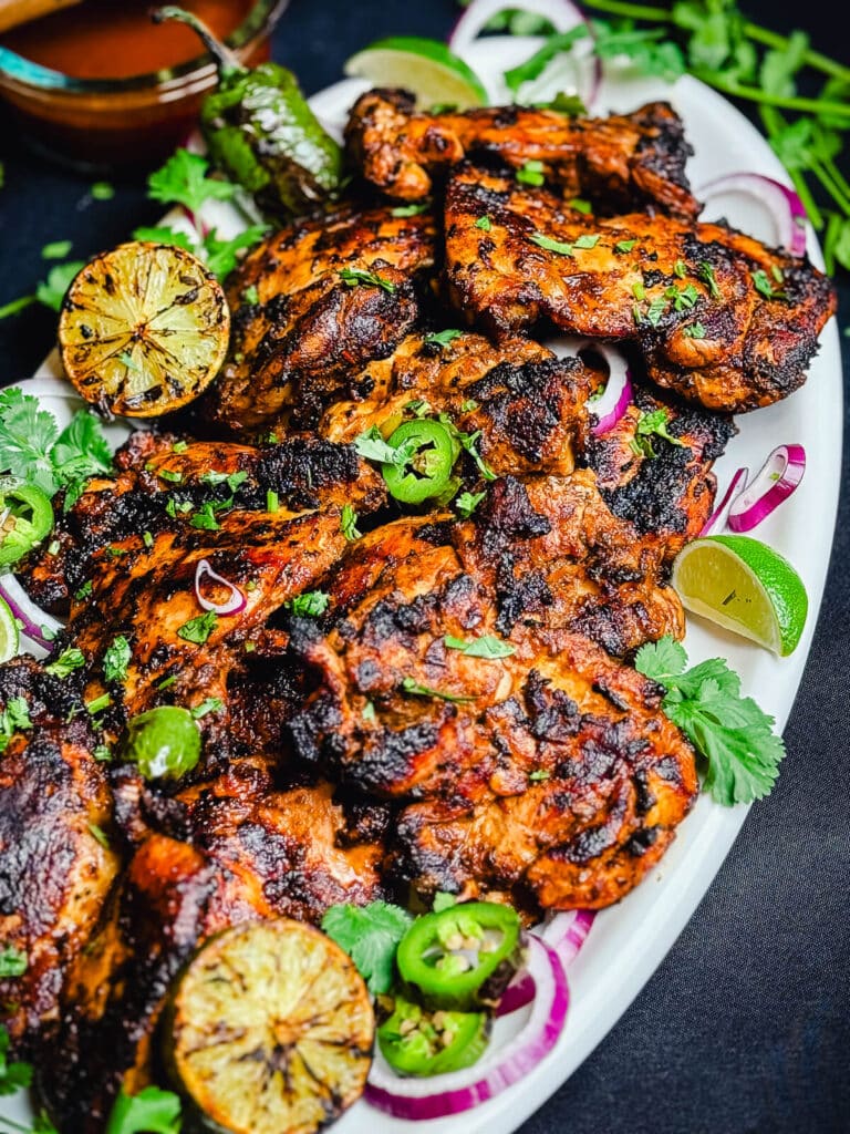 white platter full of chipotle chicken thighs, limes, and jalapeños
