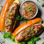 Beer brats in buns on a grey plate with whole grain mustard