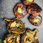 grilled ribeye steaks and artichokes on a cutting board
