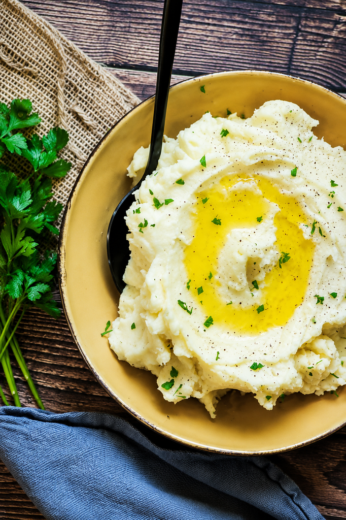 roasted garlic mashed potatoes with melted butter and parsley in a yellow bowl with black spoon