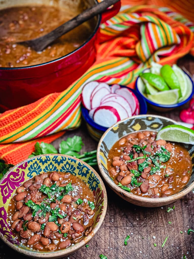 two bowls of borracho beans with condiments