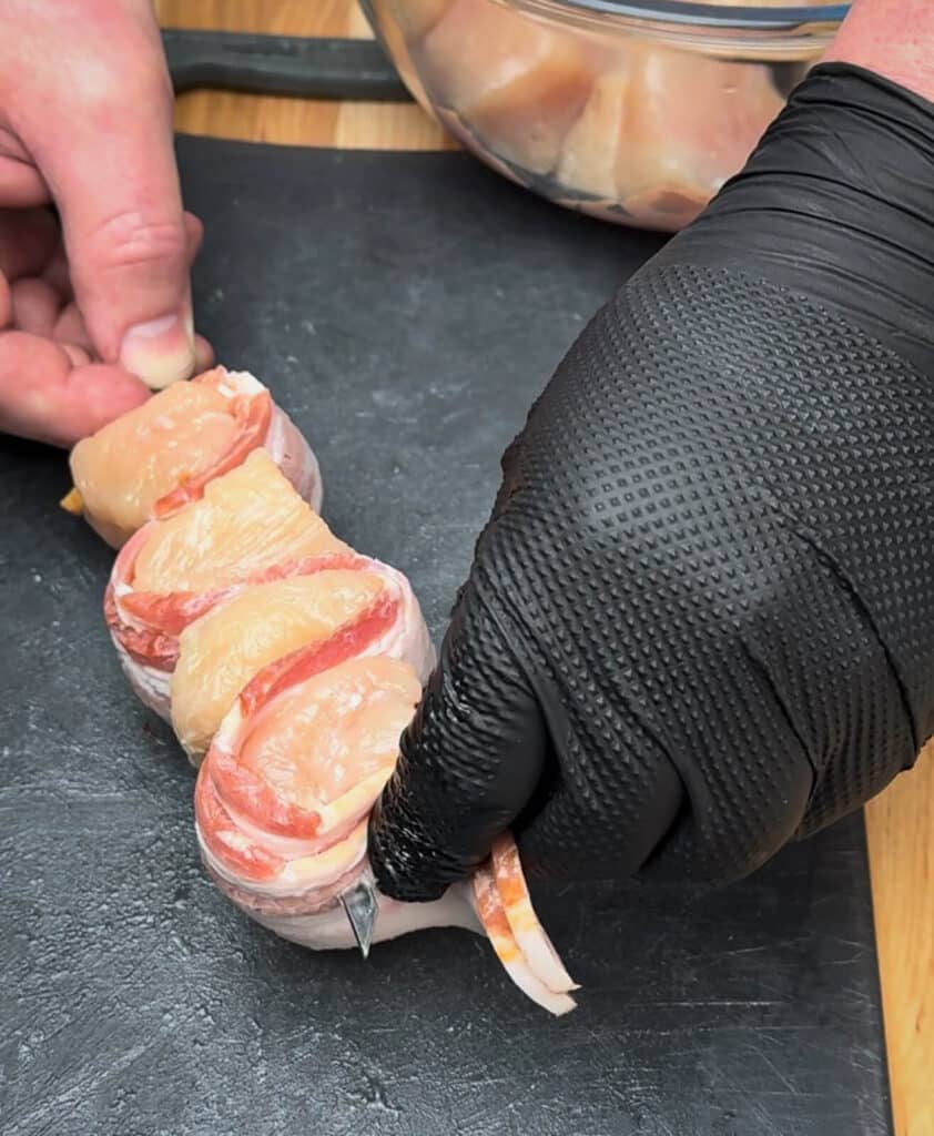 chicken being put on a skewer with bacon