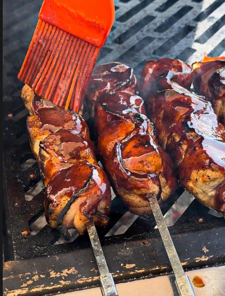 sauce being applied to chicken and bacon skewers